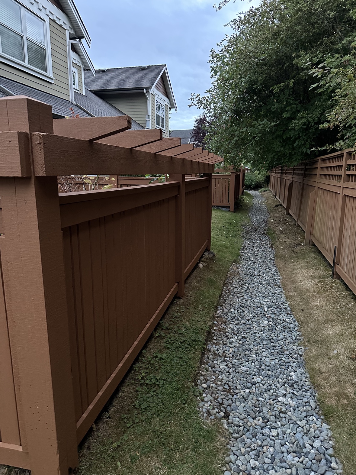 Fence painting in warm brown with pergola tops along a garden path in Victoria, BC